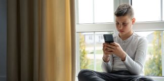 Garoto adolescente olha tela de celular sentado no chão