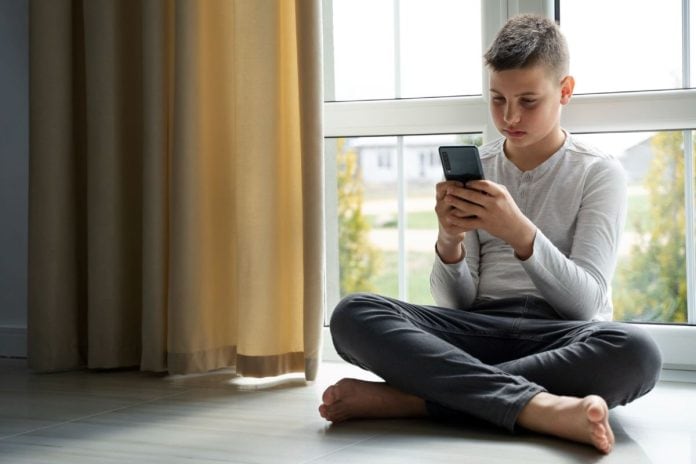 Garoto adolescente olha tela de celular sentado no chão