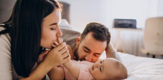 Mãe e pai brincam com bebê na cama