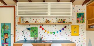 Espaço de estudos infantil com mesa eestante de madeira, bandeirolas e quadrinhos decorativos