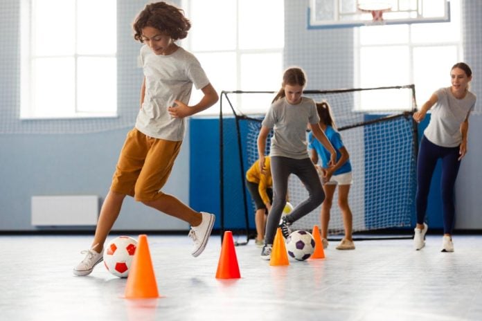 Crianças correm entre cones e bolas em quadra de esportes