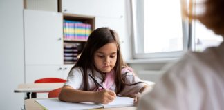 Menina de cara séria escreve em caderno na sala de aula
