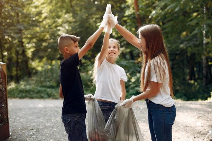 Três crianças reciclam lixo em área verde