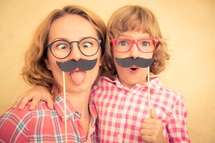 Mãe e filho seguram bigode postiço e fazem caretas engraçadas
