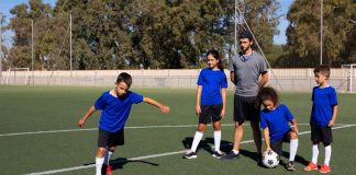 Quatro crianças e um professor treinam futebol