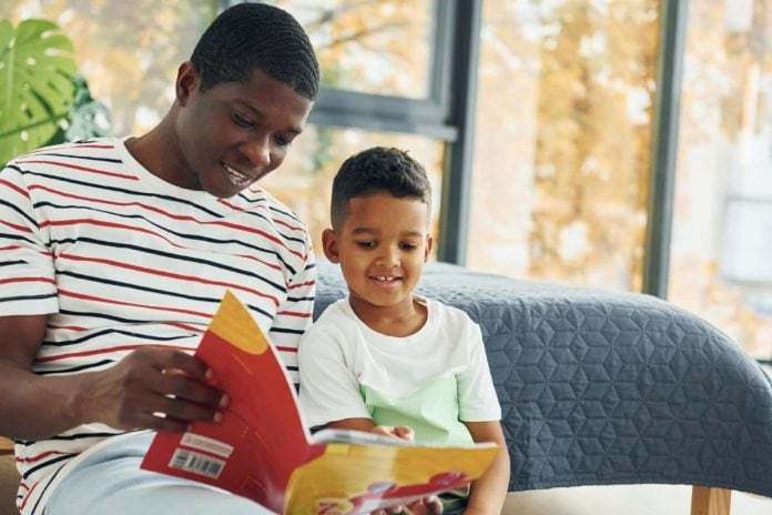 Pai lê livro infantil com o filho no sofá