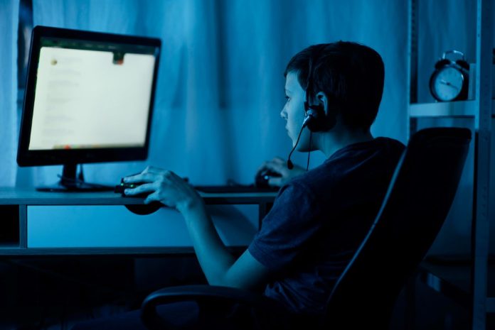 Adolescente usa computador em ambiente escuro
