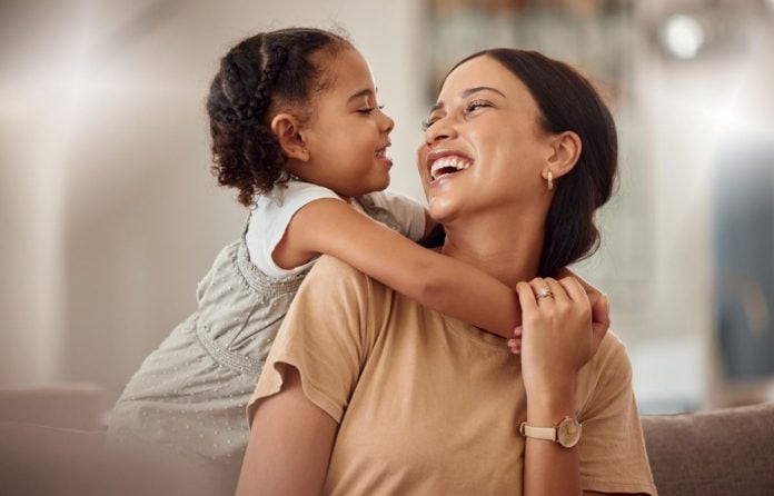 Mãe sorri para filha que a abraça pelas costas