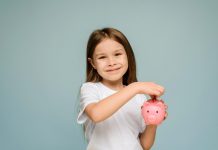 Menina sorridente coloca moeda em cofrinho rosa