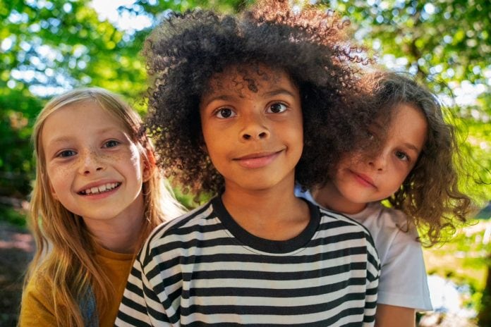 Três crianças ao ar livre, de diferentes raças