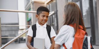 Dois alunos de mochila nas costas conversam em pé