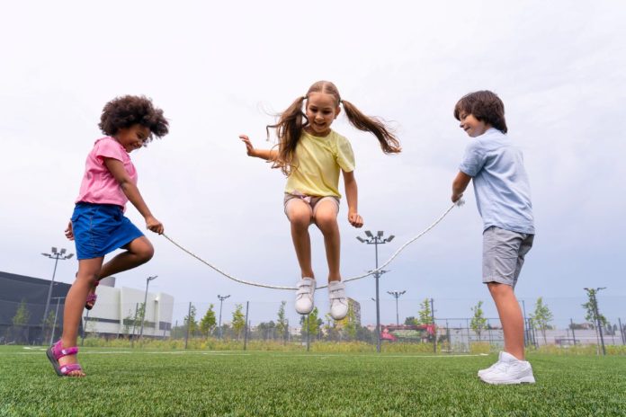 Três crianças brincam de pular corda no gramado