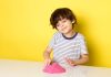 5 brincadeiras sensoriais para as crianças se divertirem; menino em fundo amarelo brincando com massinha rosa