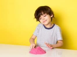5 brincadeiras sensoriais para as crianças se divertirem; menino em fundo amarelo brincando com massinha rosa