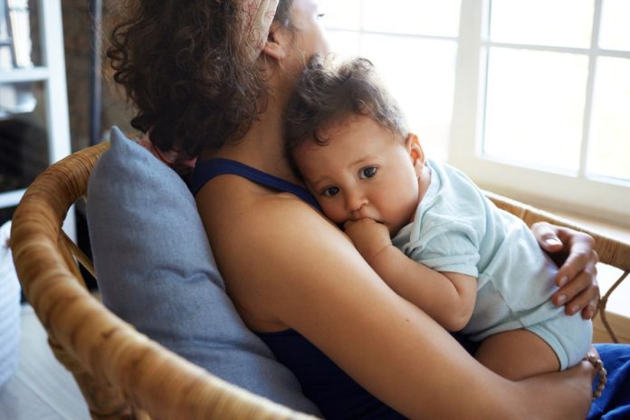Mãe está sentada com bebê no colo; nascimento do beê pode provocar condições como o baby blues ou a depressão pós-parto