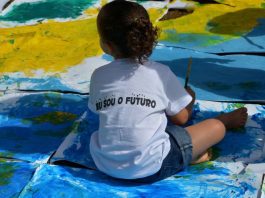 Menina está sentada sobre cartolinas pintadas com as cores do Brasil