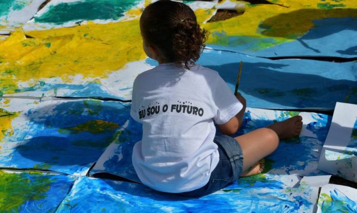 Menina está sentada sobre cartolinas pintadas com as cores do Brasil