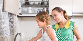 Filhos que participam de tarefas domésticas são mais bem-sucedidos; menina ajudando a mãe a lavar a louça