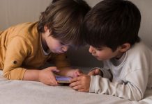 Dois meninos olham para tela de celular na cama