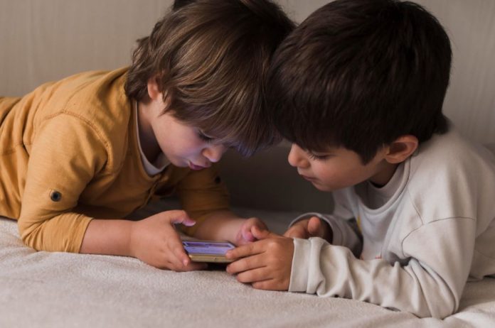 Dois meninos olham para tela de celular na cama