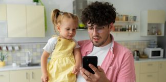 Pai segura filhos nos braços e olha para tela de celular