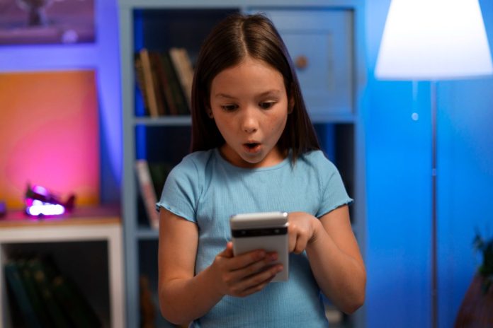 Criança faz cara de espanto ao olhar para tela de celular