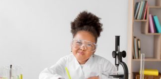 Menina com óculos de cientista faz experimentos na mesa