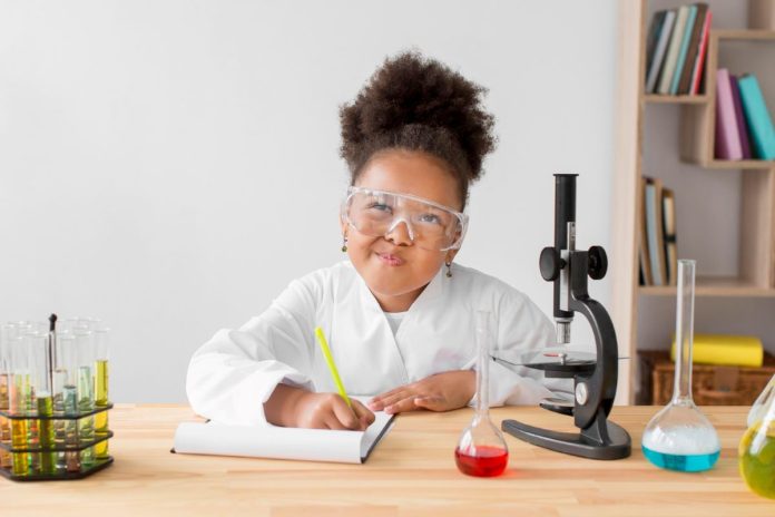 Menina com óculos de cientista faz experimentos na mesa