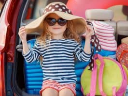 Menina de chapéu e óculos de sol no porta mala do carro