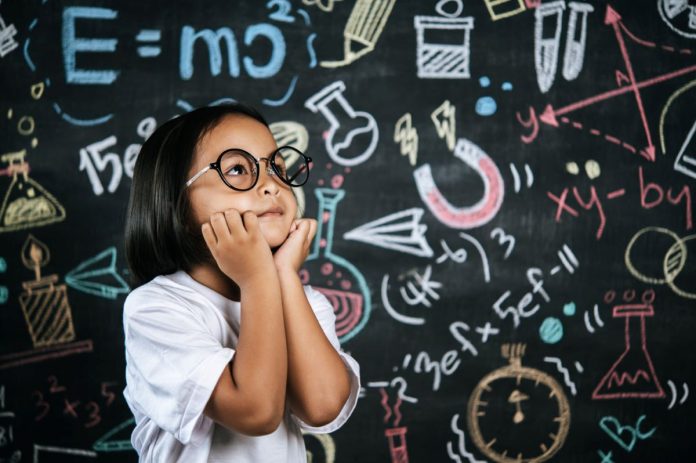 Menina de óculos em frente a lousa com cálculos matemáticos
