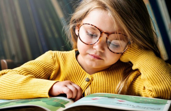 Menina de óculos lê livros durante processo de alfabetização