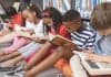 Crianças leem livros sentadas no chão de biblioteca