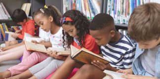 Crianças leem livros sentadas no chão de biblioteca