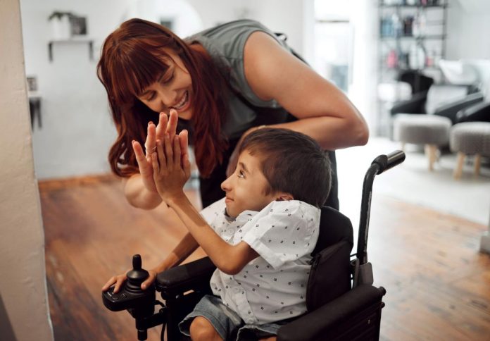 Mãe brinca com filho com deficiência em cadeira de rodas