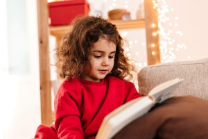 Menina de blusa vermelha lê obra; livros são uma boa opção de presente para o Natal