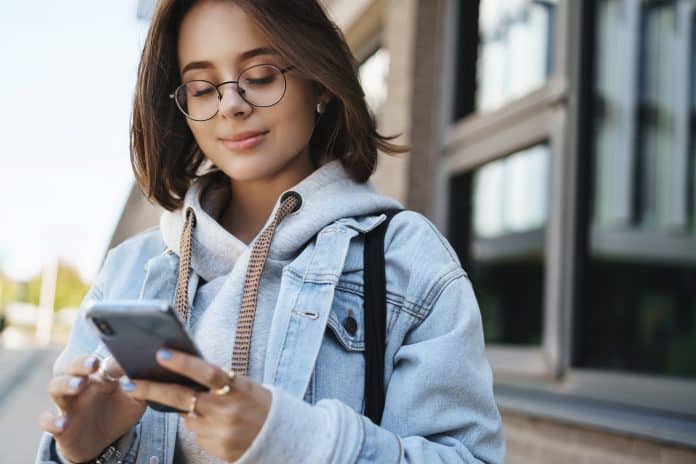 Menina olhando para celular e sorrindo; 1 em cada 5 adolescentes usa redes sociais, diz pesquisa