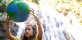 Menina segura globo terrestre com as mãos ao alto em frente a cachoeira
