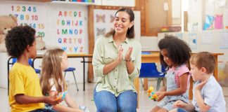 Professora com os alunos no chão cantando; Crianças só brincam ou também aprendem na Educação Infantil?