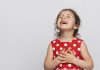 Menina com vestido de bolinha vermelho e branco com a mão no coração sorrindo; 5 dicas para incentivar a gratidão nas crianças