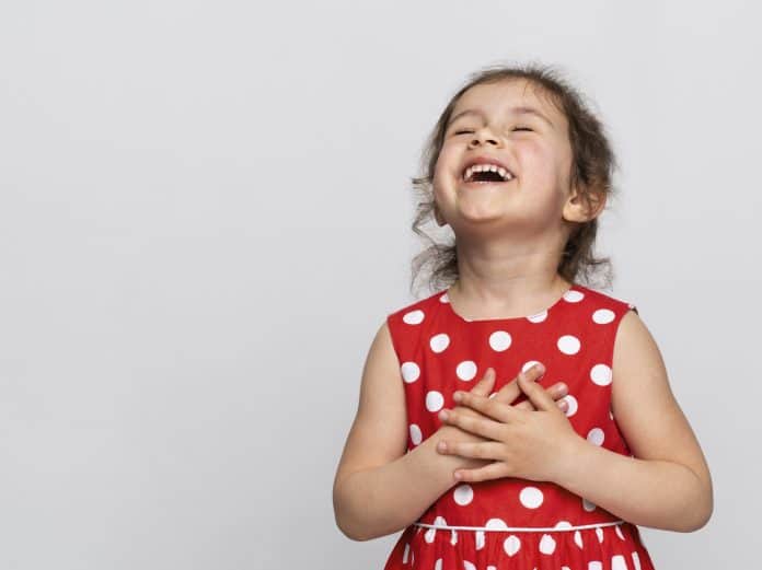 Menina com vestido de bolinha vermelho e branco com a mão no coração sorrindo; 5 dicas para incentivar a gratidão nas crianças