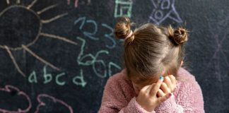 Menina esconde rosto em frente à lousa de sala de aula escolar
