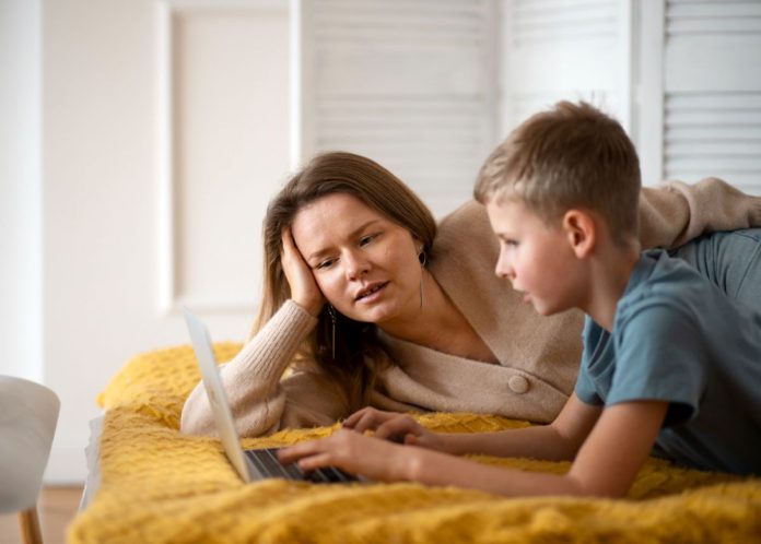 Mãe lê algo no laptop com o filho; pais devem servir de exemplo quanto a práticas de inclusão para os filhos