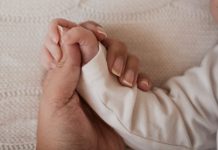 Mão de adulto segura mãe de bebê recém-nascido