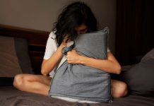 Adolescente com ansiedade abraça travesseiro na cama