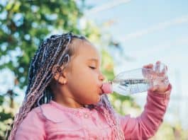 Criança de tranças em cabelo afro bebe água em garrafa