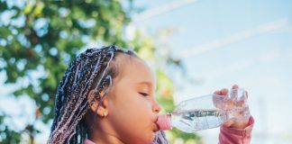Criança de tranças em cabelo afro bebe água em garrafa