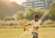 Menino brinca com aviãozinho de madeira ao ar livre