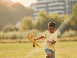 Menino brinca com aviãozinho de madeira ao ar livre