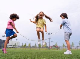 Três crianças brincam de pular corda em área ao ar livre