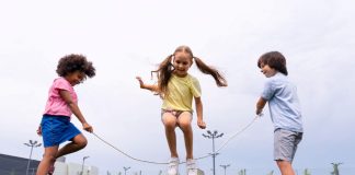 Três crianças brincam de pular corda em área ao ar livre